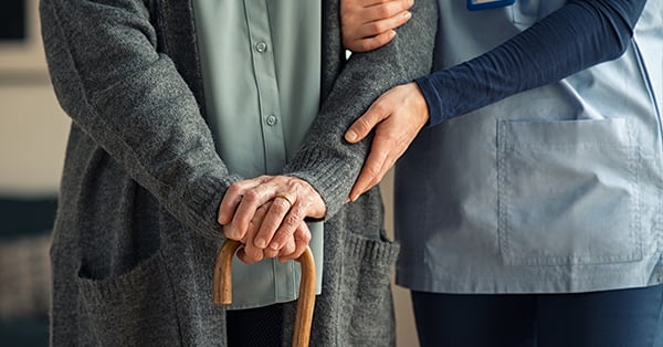 Image of eldery person holding a cane and  another person holding their arm